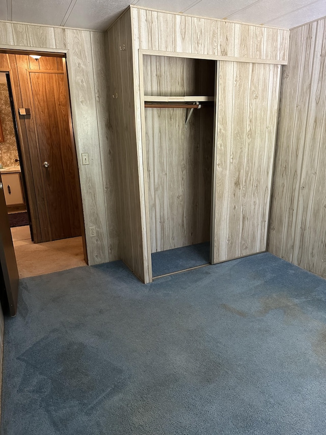 unfurnished bedroom featuring wood walls, a closet, carpet floors, and a textured ceiling