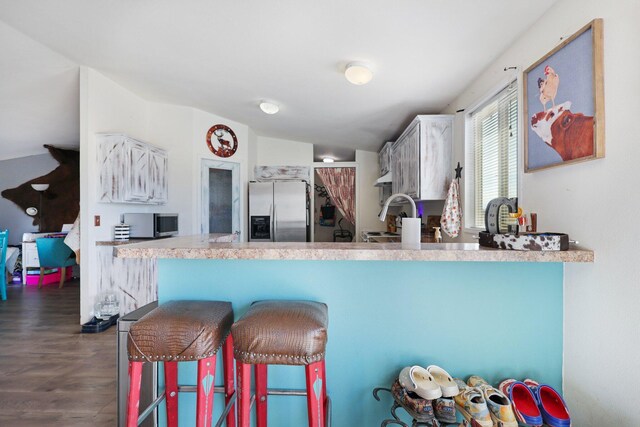 kitchen with stainless steel appliances, dark hardwood / wood-style flooring, kitchen peninsula, lofted ceiling, and a breakfast bar area