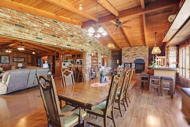 dining area with ceiling fan with notable chandelier, wood walls, and vaulted ceiling with beams