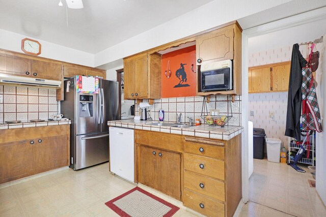 kitchen with tasteful backsplash, stainless steel appliances, tile counters, sink, and ceiling fan