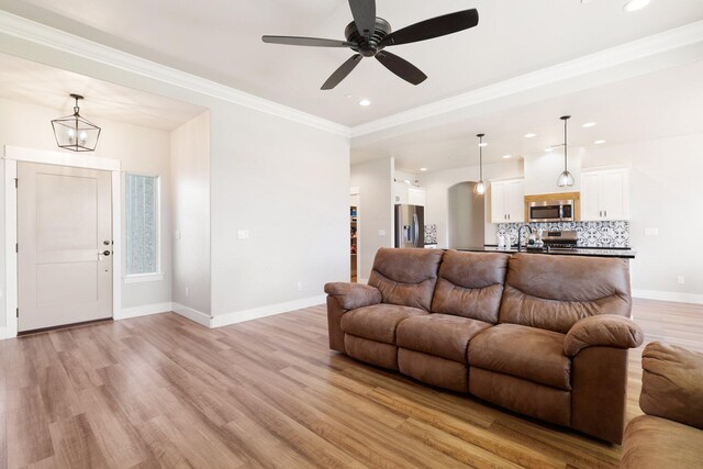 living room featuring ceiling fan, sink, crown molding, and light hardwood / wood-style flooring