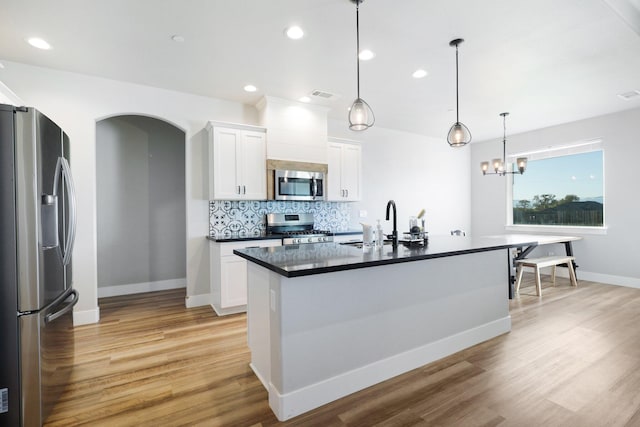 kitchen featuring a kitchen island with sink, stainless steel appliances, white cabinets, and hanging light fixtures