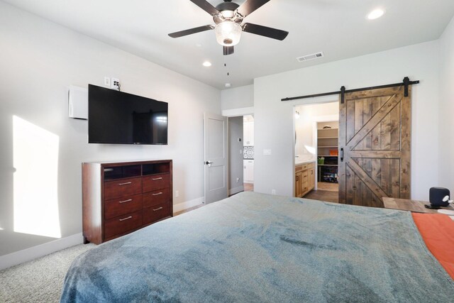 carpeted bedroom featuring a barn door, ceiling fan, and ensuite bathroom