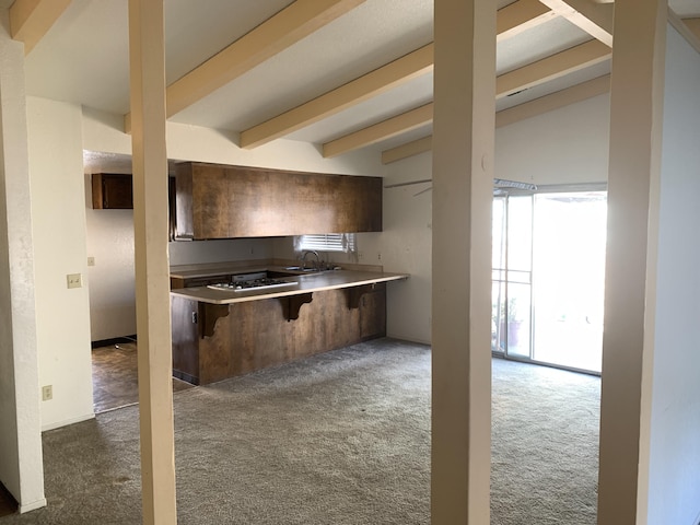 kitchen with carpet, beam ceiling, a peninsula, a sink, and a kitchen breakfast bar