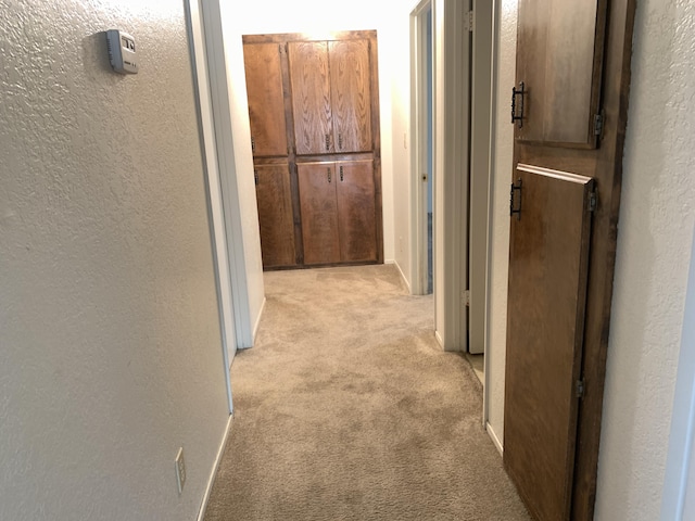 corridor with a textured wall, baseboards, and light carpet