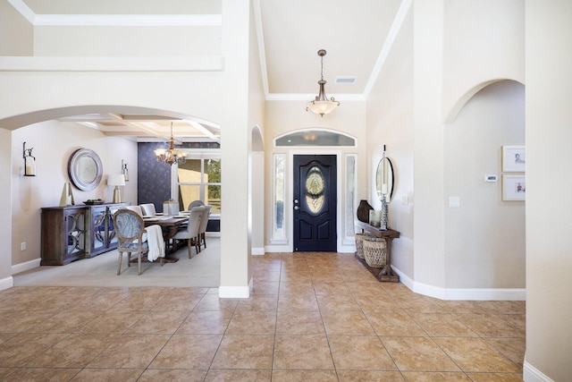 tiled entryway with a notable chandelier, ornamental molding, beamed ceiling, and a high ceiling