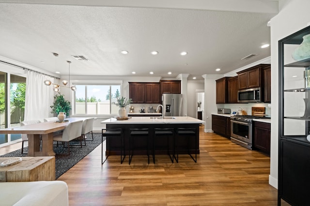 kitchen with appliances with stainless steel finishes, a kitchen bar, hanging light fixtures, and light hardwood / wood-style floors