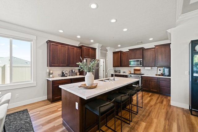 kitchen featuring light wood-type flooring, stainless steel appliances, sink, a breakfast bar area, and a kitchen island with sink