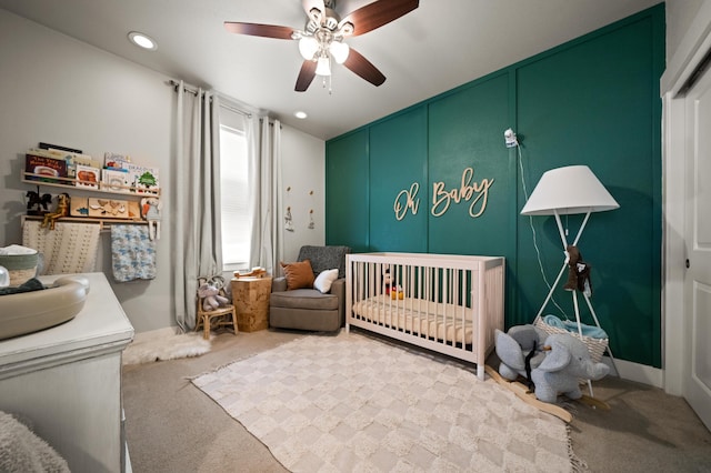 carpeted bedroom with ceiling fan and a crib