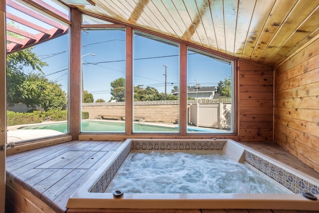 unfurnished sunroom featuring lofted ceiling with skylight, a healthy amount of sunlight, wooden ceiling, and a hot tub