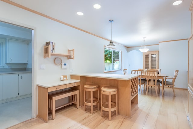 kitchen with decorative light fixtures, light hardwood / wood-style floors, crown molding, a breakfast bar, and kitchen peninsula