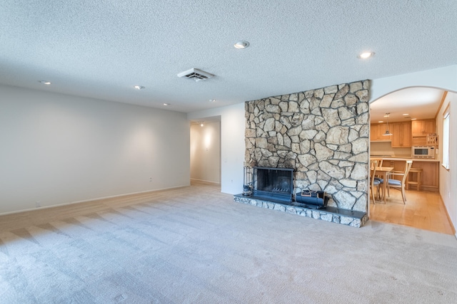 carpeted living room featuring a textured ceiling and a stone fireplace