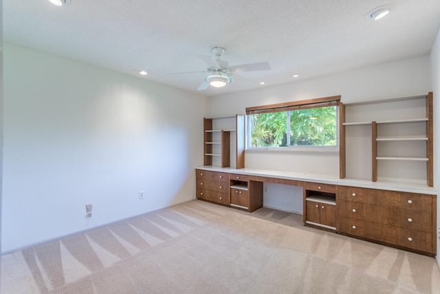 unfurnished office featuring built in desk, ceiling fan, light carpet, and a textured ceiling