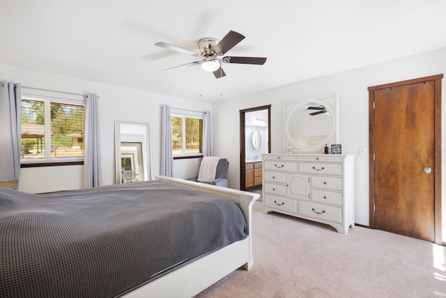 bedroom with multiple windows, light colored carpet, ensuite bathroom, and ceiling fan