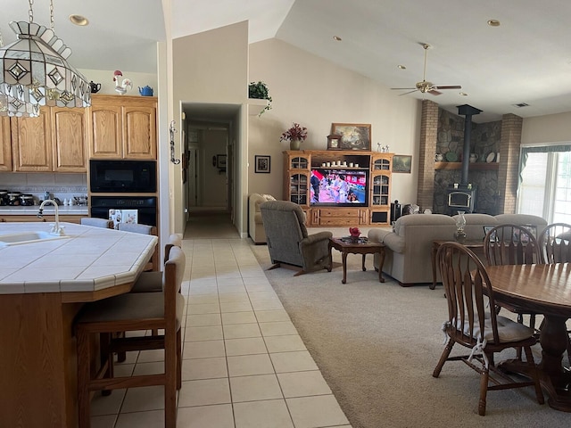 dining room with light colored carpet, a wood stove, ceiling fan, sink, and high vaulted ceiling