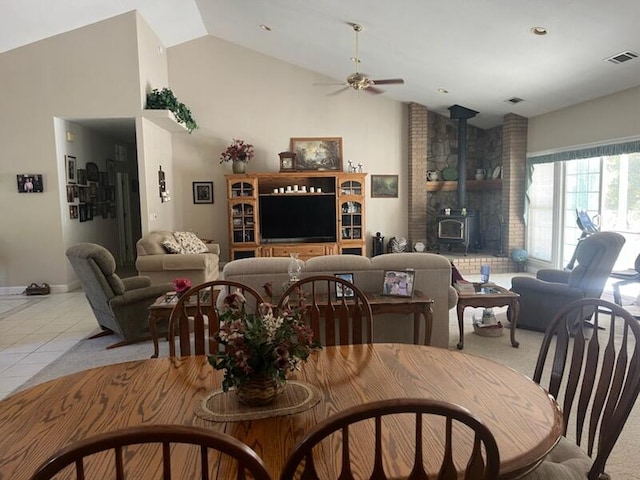 dining area with vaulted ceiling, light tile patterned flooring, ceiling fan, and a wood stove