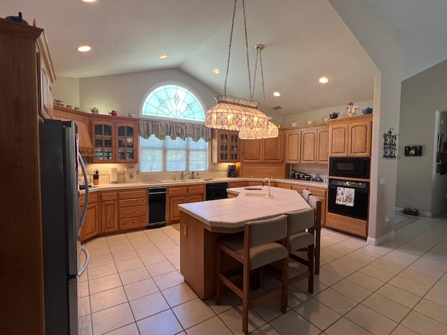 kitchen featuring tile countertops, black appliances, lofted ceiling, a center island with sink, and light tile patterned flooring