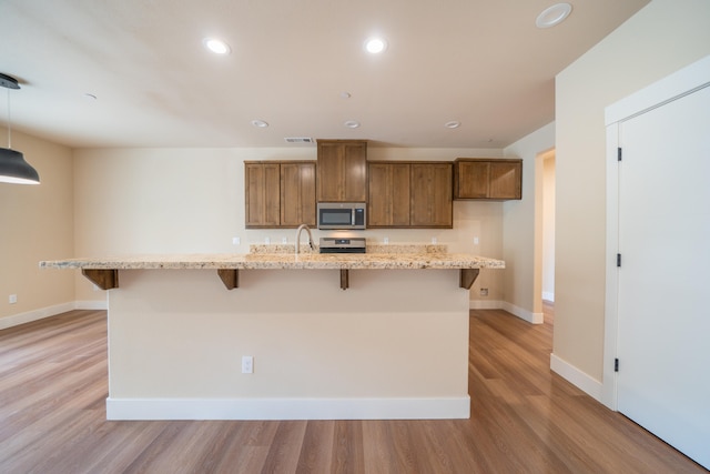 kitchen featuring pendant lighting, light hardwood / wood-style floors, a kitchen bar, a center island with sink, and appliances with stainless steel finishes