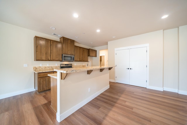 kitchen featuring light stone counters, a center island with sink, light hardwood / wood-style flooring, stainless steel appliances, and a breakfast bar area