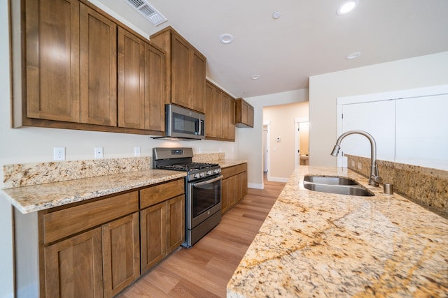 kitchen featuring light stone countertops, stainless steel appliances, light wood-type flooring, and sink