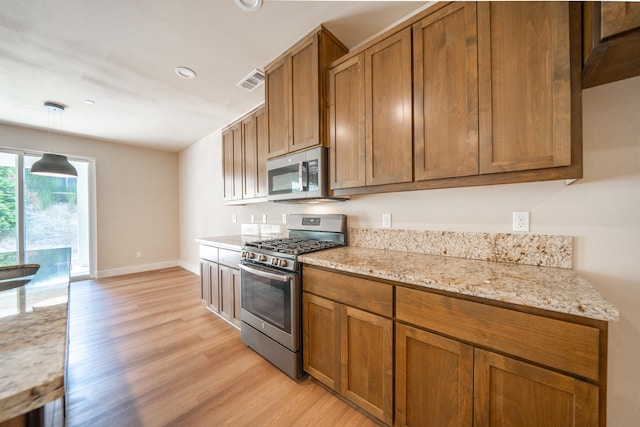 kitchen with hanging light fixtures, light stone countertops, light hardwood / wood-style flooring, and stainless steel appliances