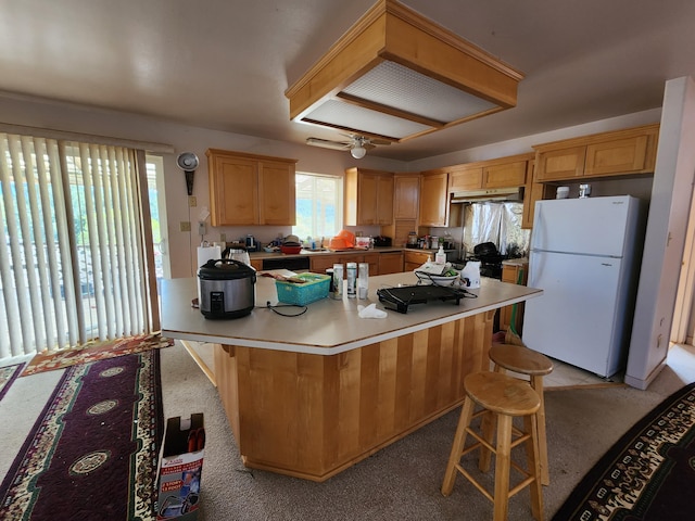 kitchen with light carpet, a kitchen bar, a center island, and white fridge