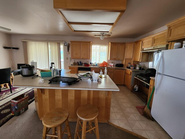 kitchen with light tile patterned floors, dishwasher, white refrigerator, a breakfast bar area, and a kitchen island