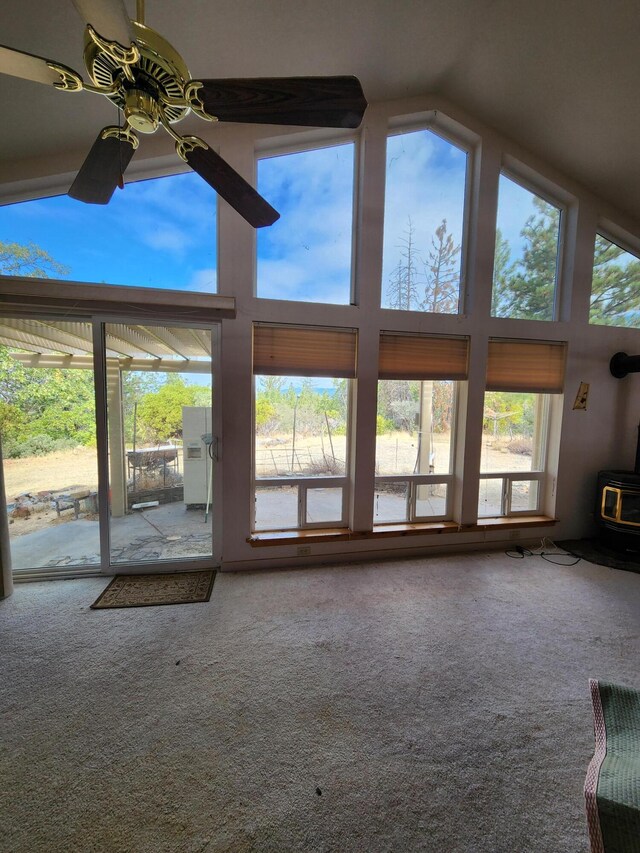 unfurnished living room featuring vaulted ceiling, a wood stove, ceiling fan, and carpet floors