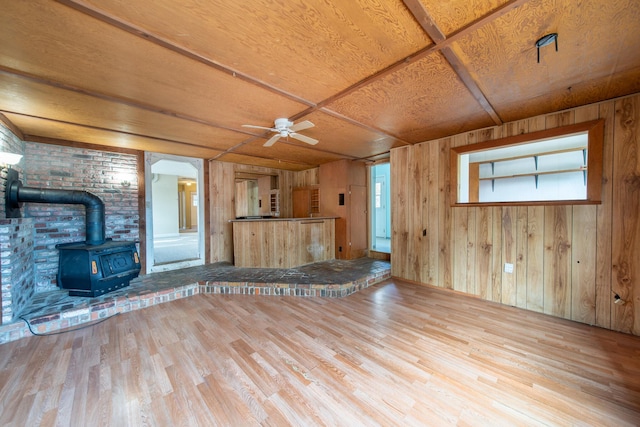 unfurnished living room featuring a wood stove, wooden walls, hardwood / wood-style flooring, ceiling fan, and wood ceiling