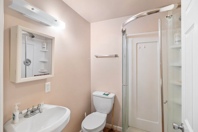 bathroom featuring toilet, a shower with shower door, and sink