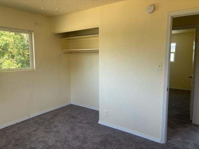 unfurnished bedroom with dark carpet, a textured ceiling, and a closet