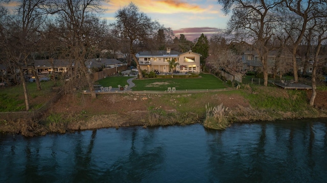 back house at dusk with a yard and a water view