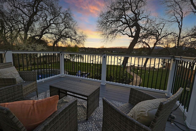 deck at dusk with an outdoor living space, a yard, and a water view