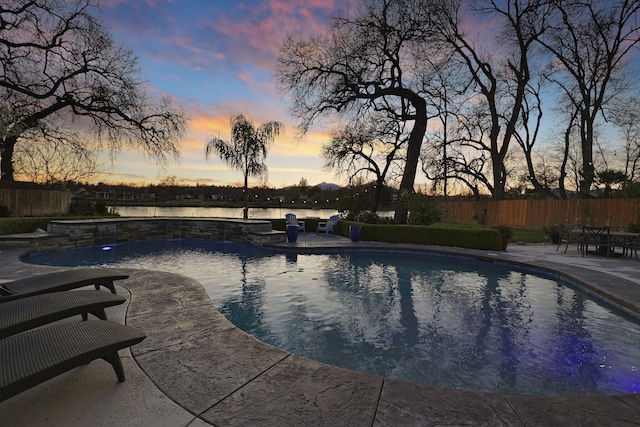 pool at dusk with pool water feature, a water view, and a patio area