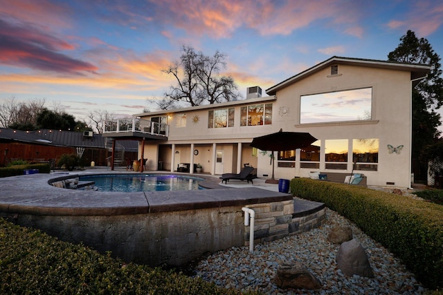 back house at dusk with a balcony, a fenced in pool, and a patio