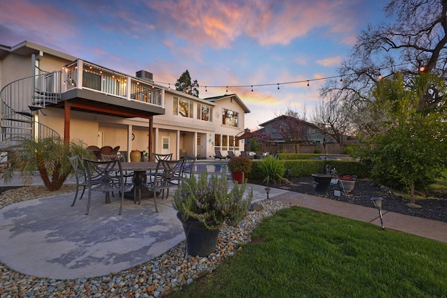 back house at dusk featuring a yard, a balcony, and a patio area