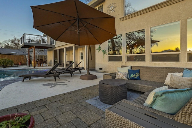 patio terrace at dusk with a balcony, an outdoor living space, and a fenced in pool