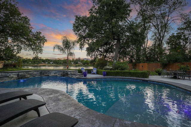 pool at dusk with a patio area and pool water feature