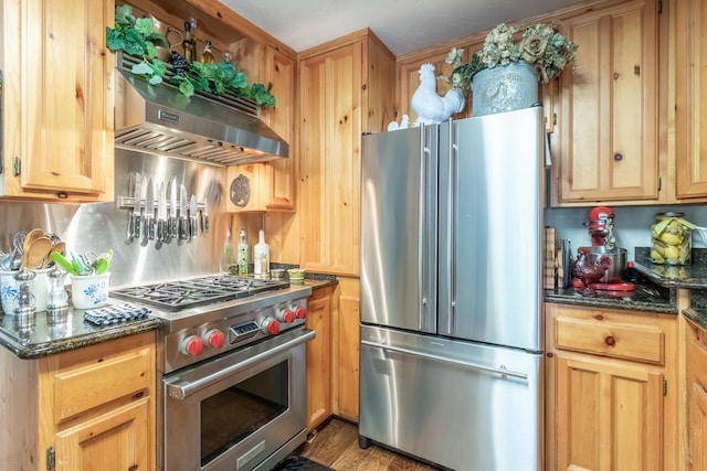 kitchen featuring stainless steel appliances, light hardwood / wood-style floors, dark stone counters, and wall chimney range hood