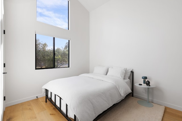 bedroom with baseboards, vaulted ceiling, and light wood finished floors