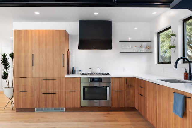 kitchen with range hood, light countertops, a sink, modern cabinets, and oven