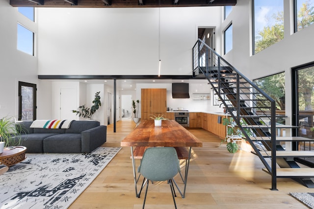 living room featuring a towering ceiling, light wood finished floors, plenty of natural light, and stairs