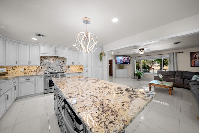 kitchen with ceiling fan with notable chandelier, high end stove, white cabinetry, and a kitchen island