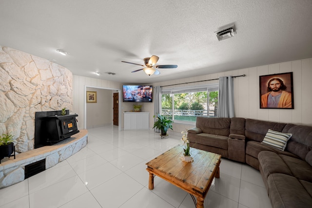 living room with a wood stove, ceiling fan, light tile patterned floors, and a textured ceiling