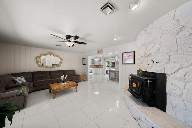 living room featuring wood walls, ceiling fan, a wood stove, and tile patterned floors