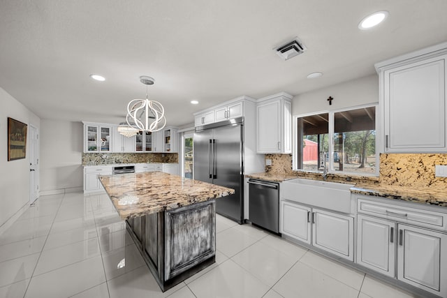 kitchen with a chandelier, white cabinets, a kitchen island, backsplash, and appliances with stainless steel finishes