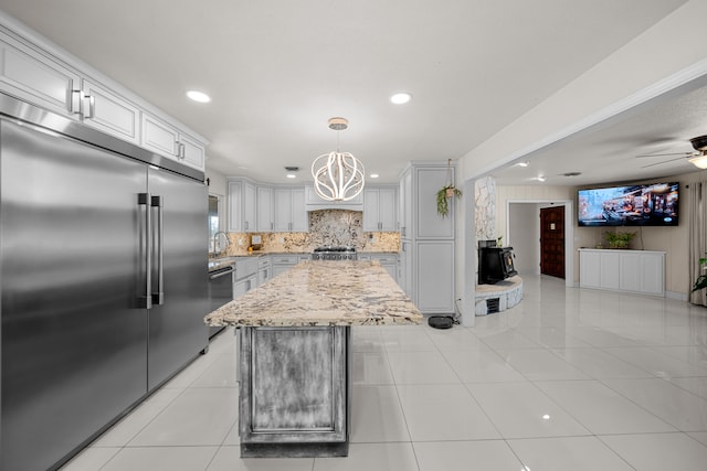 kitchen featuring ceiling fan with notable chandelier, backsplash, stainless steel appliances, a center island, and decorative light fixtures