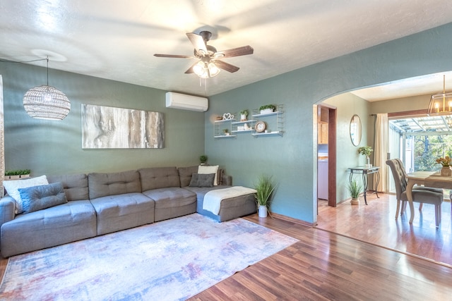 living room featuring hardwood / wood-style flooring, ceiling fan with notable chandelier, and a wall unit AC