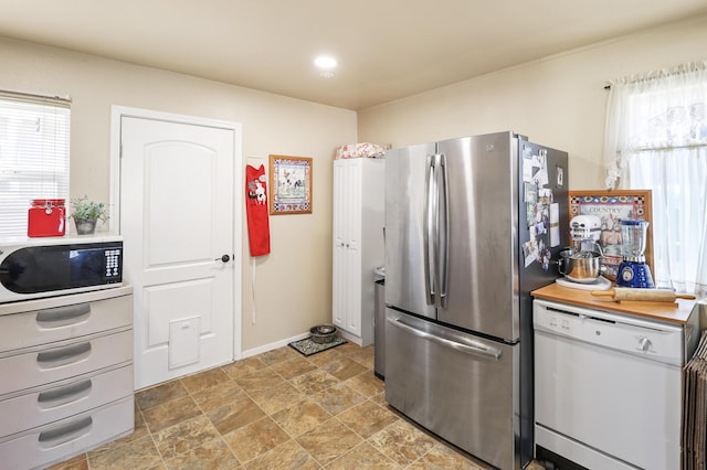 kitchen with light countertops, stone finish floor, dishwasher, baseboards, and freestanding refrigerator