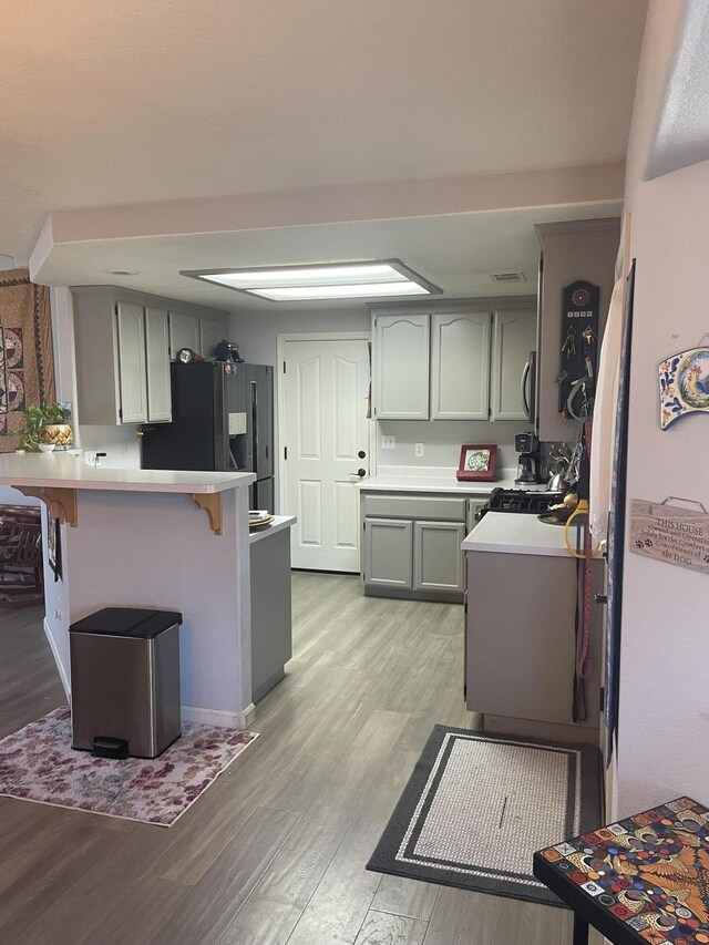 kitchen featuring a kitchen bar, black refrigerator with ice dispenser, light hardwood / wood-style flooring, and kitchen peninsula